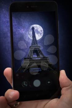 videobloger takes pictures on a smartphone.  Eiffel Tower in Paris, France. The stars and the moon shine at night.