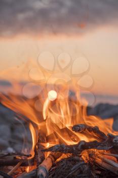 A fire burns near the sea at sunset.