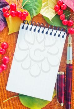 autumn leaves and notepad on wooden background