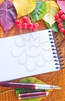 autumn leaves and notepad on wooden background