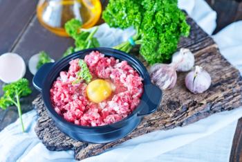 minced meat and raw egg in bowl and on a table
