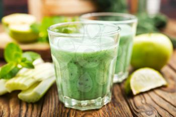 Glass of green vegetable smoothie. Green vegetable smoothie and ingredients: celery avocado cucumber kiwi apple banana lemon and herbs