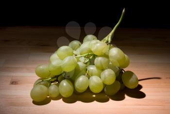 Green grapes bunch on a wooden table in the dark