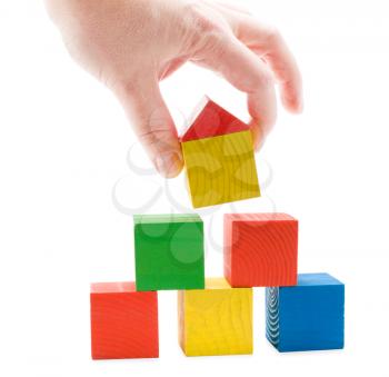 Hand establishes toy house on the wooden cubes pyramid. Isolated on white background.