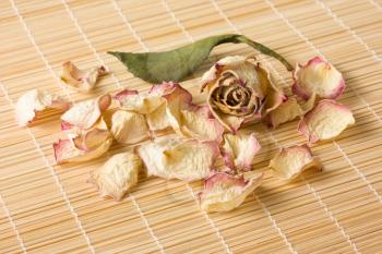 Dried rose flower, petals and leaf lie on a reed mat close-up view