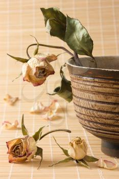 Dry rose with wilted green leaves in an old wooden bowl and dried rosebuds and petals on a straw mat