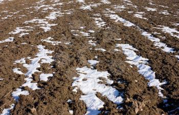 Plowed field under the melting snow under bright sunlight in spring
