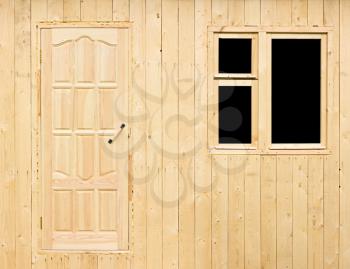 Wooden wall of the rural house under construction made of the rough raw boards with the unfinished door and a window without platbands