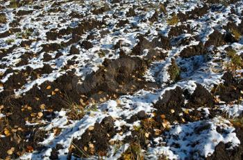 First snow on plowed soil textured surface with grooves under bright sunlight