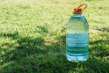 Big plastic bottle with fresh cold blue water on green grass lawn in shadow under bright summer sunlight
