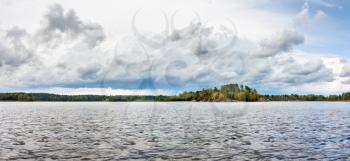 Natural panorama north summer landscape - Ladoga lake with lake shore with green trees on the horizon under cloudy sky with white clouds in overcast day panoramic view