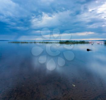 Blue dramatic minimalist landscape with smooth surface of the lake with calm water with horizon under dramatic cloudy sky, simple beautiful calm natural blue background