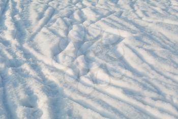 Surface of pure white snow with chaotic tracks with shiny snowflakes under bright sunlight perspective view, winter abstract natural background
