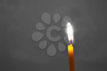 One burning candle on a gray background