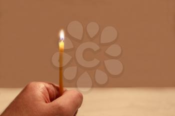 The hand holding a burning candle on a beige background