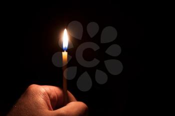The hand holding a burning candle on a dark background