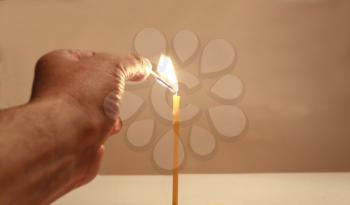 Hand with a match ignites a candle in warm colors