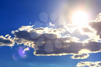 Bright sun on blue sky with gray clouds