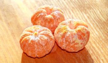 Three peeled mandarin in the rays of light on a wooden background