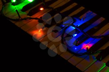 Multicolored lights of a garland on the piano on a dark background