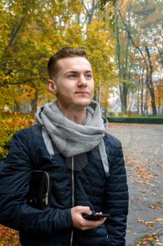 Cute young man with smartphone in autumn park