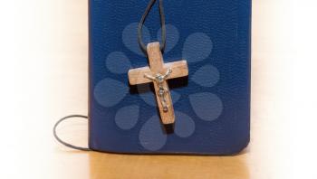 Closed book and wooden cross on a wooden surface with a light vignette