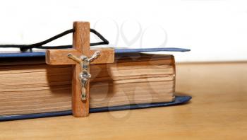 Closed book and wooden cross on a wooden surface