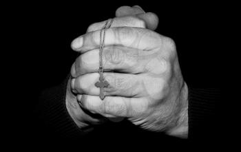 Black and white image of a hands with a cross on a dark background