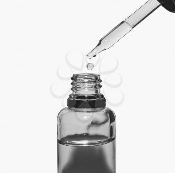 Glass bottle and pipette with a drop of liquid close up isolated on a light background