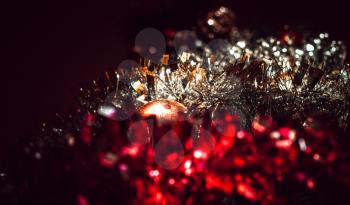 Blurred dark festive background with a warm shade from tinsel with a ball