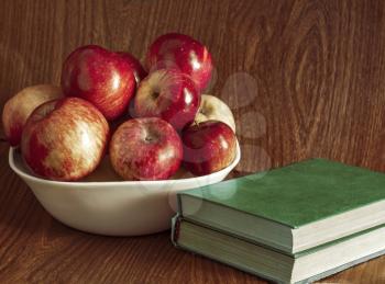 Vase with apples and books on a wooden background