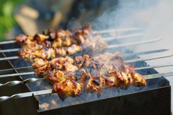 Grilling marinated shashlik with smoke. Skewered meat. Shallow depth of field. Selective focus.