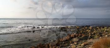 Panoramic seascape. Rocky shore in the foreground. Dramatic sky and the sea.