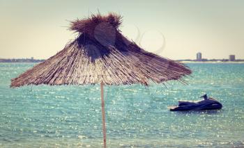 Straw beach umbrella on a background of the cloudless sky and calm sea on a bright sunny day. Toned image. Shallow depth of field.