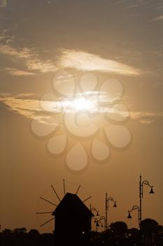 Dawn. Silhouettes of windmill and decorative lampposts. Plenty of space for text. Vintage style toned image.