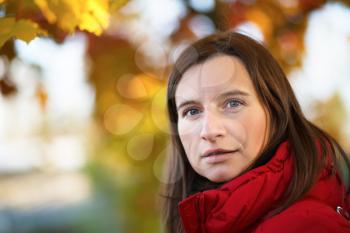 Young woman in a red jacket on a background of autumn leaves close-up. Bright colorful bokeh. Shallow depth of field. Selective focus on the near eye. Space for text.