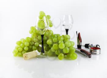 Still-life with bunch of green grapes and facilities for opening and pouring wine on a light gray background.