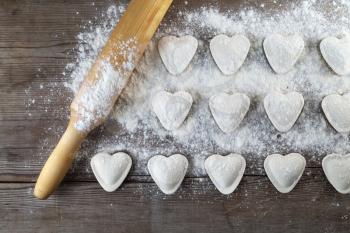Heart shaped dumplings, flour and rolling pin on wooden background. Cooking ravioli. Top view.