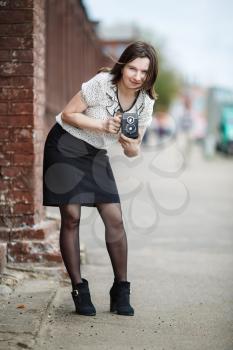 Pretty young woman with an old vintage camera in hand on a background of an old brick wall. Retro style photo. Shallow depth of field. Selective focus on model. Vertical shot.