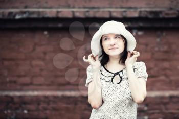 Portrait of young woman. Girl in white hat posing against blurred vintage brick wall background. Selective focus on girl. Toned photo with copy space. Vintage style photo.