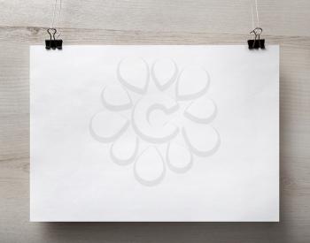 Blank white paper poster hanging on light wooden background. For design presentations and portfolios. Front view.