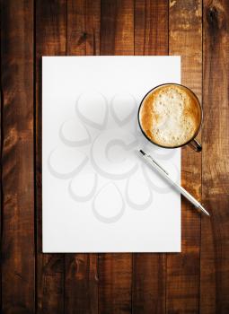 Mock-up for branding identity on vintage wooden table background. Blank letterhead, coffee cup and pen. Mock-up for design presentations and portfolios. Top view.
