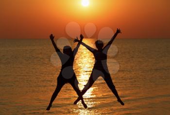 Two girls jumped on the background of the dawn sun. Focus on models. Shallow depth of field.