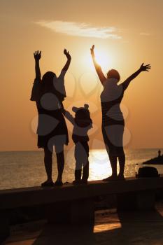 Two girls and a little girl with hands raised to meet the sunrise over the sea.  Focus on models. Shallow depth of field. Toned image.