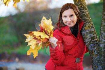 Pretty young woman in a beret and red jacket with autumn yellow maple leaf in his hand. Shallow depth of field. Selective focus on model.