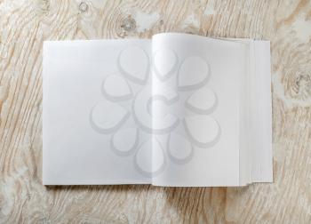 Blank opened book on light wooden background with soft shadows. Mock-up for graphic designers portfolios. Top view.