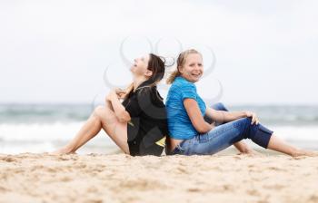 Two pretty young smiling women sitting and relaxing on the sand on the seashore. Two girls resting on the beach. Two cheerful young woman outdoors. Selective focus on the models.