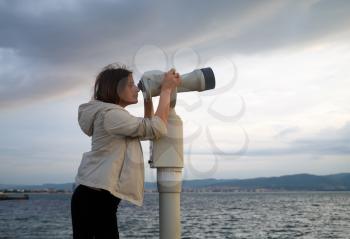 Pretty young woman using a coin operated binocular enjoying a great view of the Black sea. Early morning. Shallow depth of field. Focus on the model.
