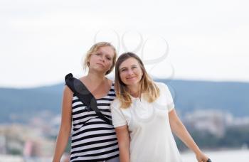 Two attractive young women outdoor. Mountains on blurred background. Shallow depth of field. Focus on models.