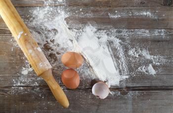 Baking background with eggs, eggshells, flour and rolling pin. Wooden background. Top view.